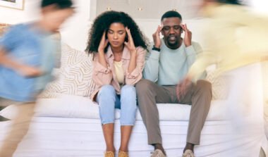 Tired parents on sofa with motion blur of energy as children run around house